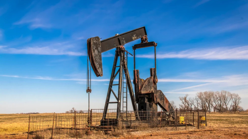 Onshore oil pumpjack at a fenced well site in a rural landscape