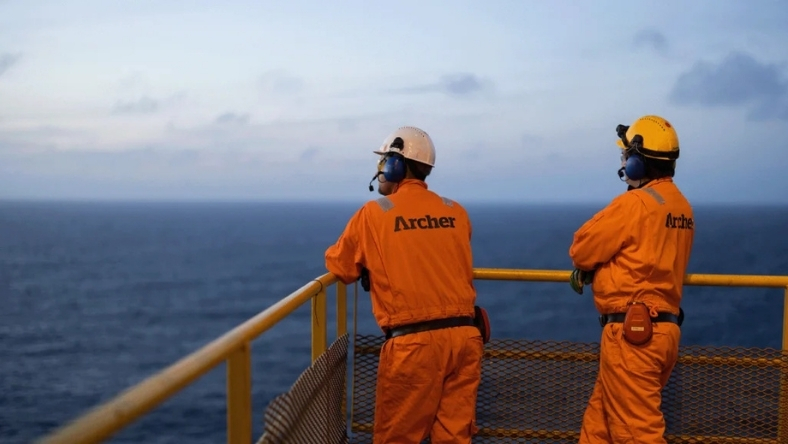 Offshore workers in orange safety gear on platform overlooking the sea