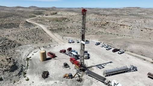 Aerial view of an oil drilling rig on an arid desert plateau surrounded by service vehicles and equipment