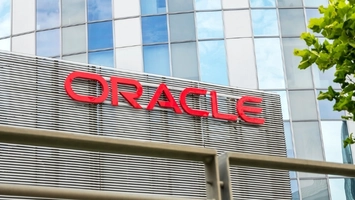 Oracle logo in red on a grey striped building with a glass office tower and green foliage in the foreground