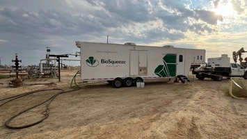 Mobile BioSqueeze treatment trailer on an active oilfield site surrounded by wellheads and field equipment