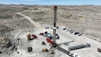 Aerial view of an oil drilling rig on an arid desert plateau surrounded by service vehicles and equipment