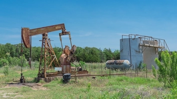Oil pumpjack operating beside storage tanks in a grassy field
